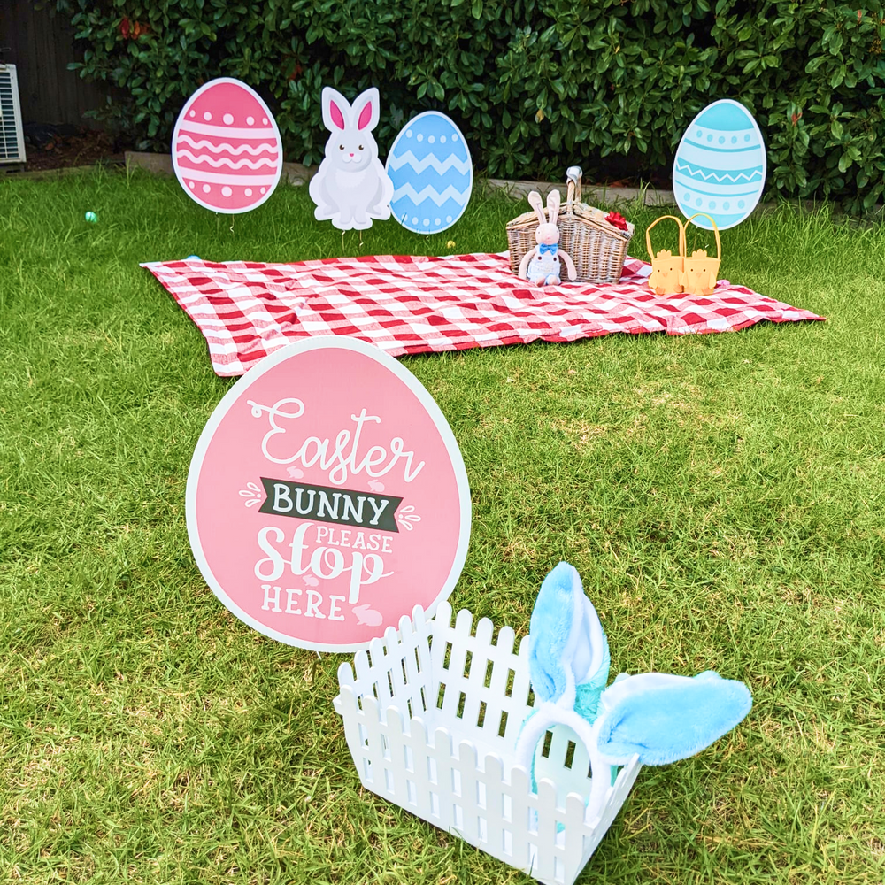 Easter egg and bunny cutouts staked into a lawn beside a picnic rug