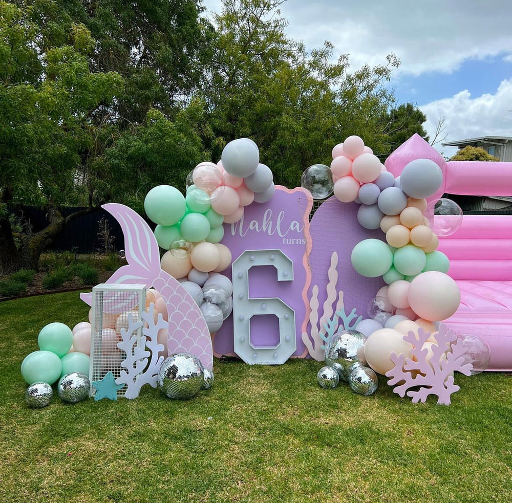 Pastel mermaid party setup with corflute cutouts and balloon garland on the lawn